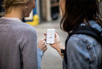 Two tourists in New York look at their phone and wait for a Lyft driver to arrive